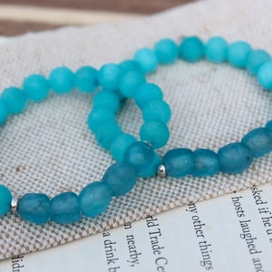 May include: Two turquoise blue beaded bracelets with silver accents. The bracelets are made of frosted glass beads and are stacked on top of each other.