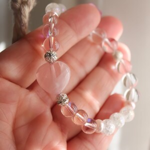 May include: A pink heart-shaped crystal charm bracelet with clear and iridescent beads. The bracelet is made with silver-toned metal accents.