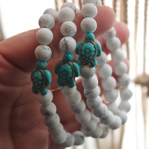 May include: Three white Howlite beaded bracelets with turquoise turtle charms. The bracelets are stacked on top of each other.