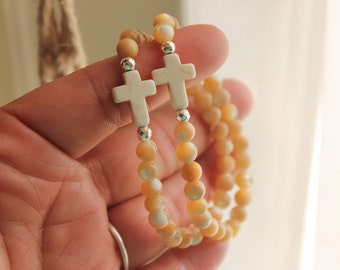 Op de afbeelding: Twee armbanden met witte kruisbedels en beige en witte kralen.