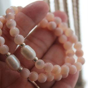 May include: Two bracelets made of pink and white beads. The bracelets are layered on top of each other and have a pearl-like finish.