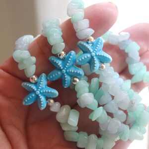 May include: A set of beaded bracelets featuring light blue and white stone chips. Each bracelet has bright blue starfish charms and small silver beads. The bracelets are designed to be worn together.