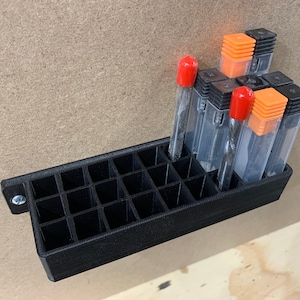 May include: A black plastic wall-mounted organizer with 24 compartments for storing small tools. The organizer has a screw on the side for mounting. There are several small tools with red and orange caps in the organizer.