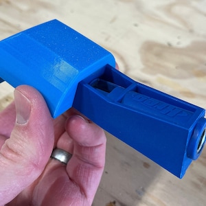 May include: A blue plastic jig with the word "Kreg" printed on the side. The jig has a small opening on the top and a round hole on the end.