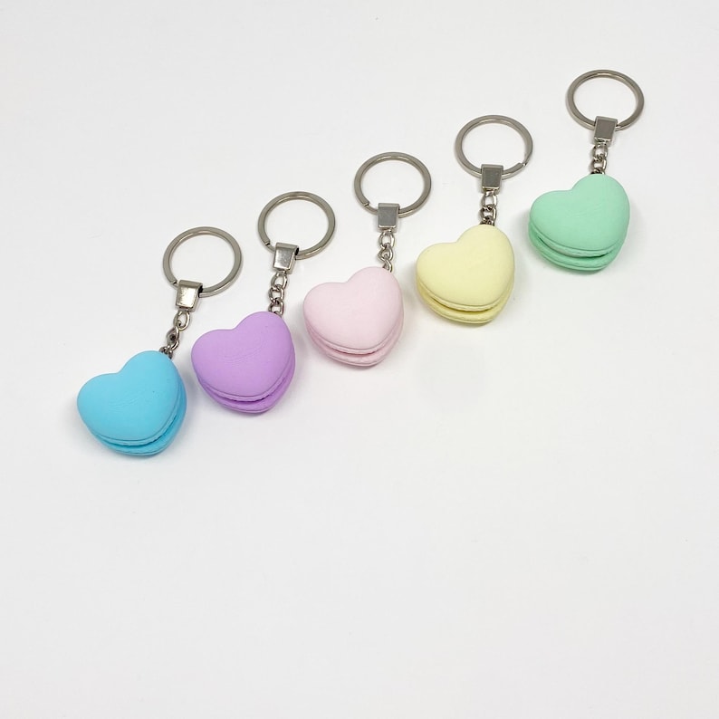 Op de afbeelding: Vijf hartvormige sleutelhangers in pasteltinten: lichtblauw, paars, roze, geel en groen. Elke hanger heeft de vorm van een macaron.