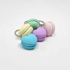 Könnte beinhalten: Ein Set aus fünf bunten Schlüsselanhängern in Macaron-Form. Die Schlüsselanhänger sind in Blautönen, Grün, Gelb, Rosa und Lila gehalten. Jeder Schlüsselanhänger hat eine weiße Füllung und eine Herzform.