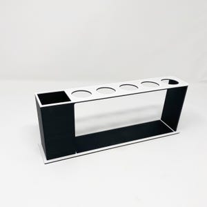 May include: A white and black organizer with five round holes and a rectangular compartment. The organizer is made of plastic and is designed to hold items such as pens, pencils, or brushes.