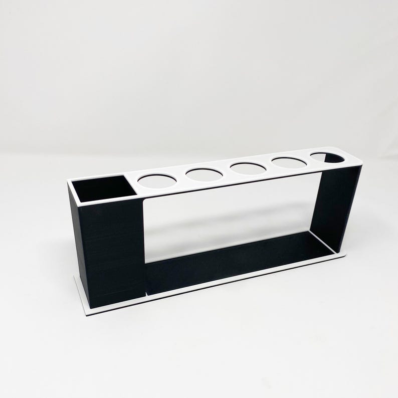 May include: A white and black organizer with five round holes and a rectangular compartment. The organizer is made of plastic and is designed to hold items such as pens, pencils, or brushes.