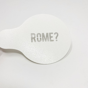 May include: White plastic stencil with the word "ROME?" cut out.