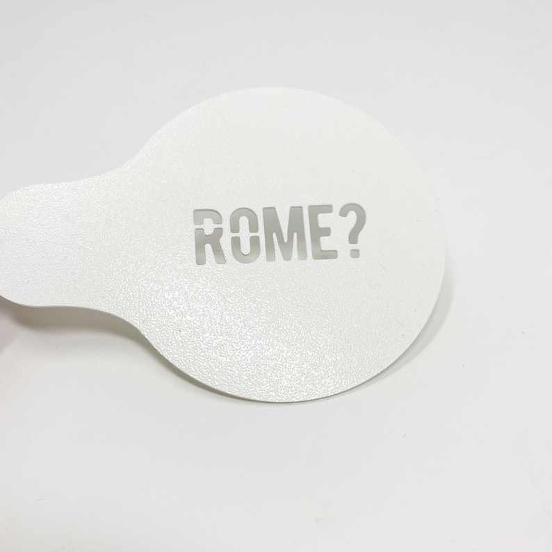May include: White plastic stencil with the word "ROME?" cut out.