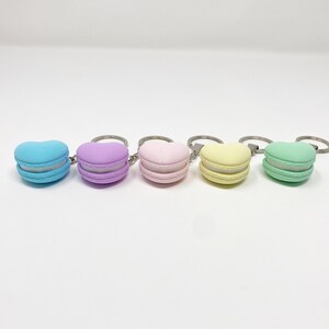 Op de afbeelding: Vijf hartvormige macaron sleutelhangers in pastelkleuren: lichtblauw, lavendel, roze, geel en groen.