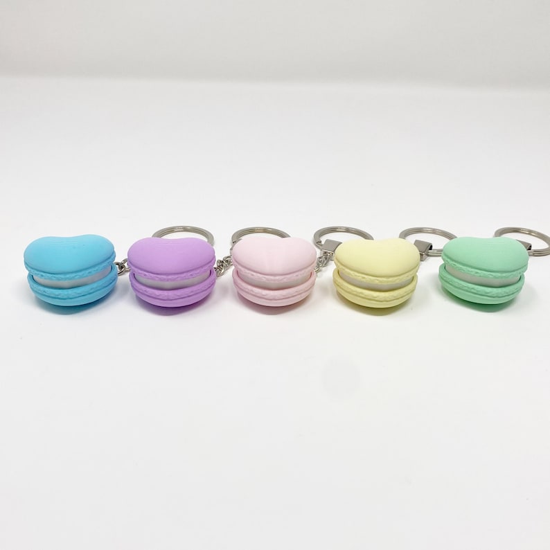 Op de afbeelding: Vijf hartvormige macaron sleutelhangers in pastelkleuren: lichtblauw, lavendel, roze, geel en groen.