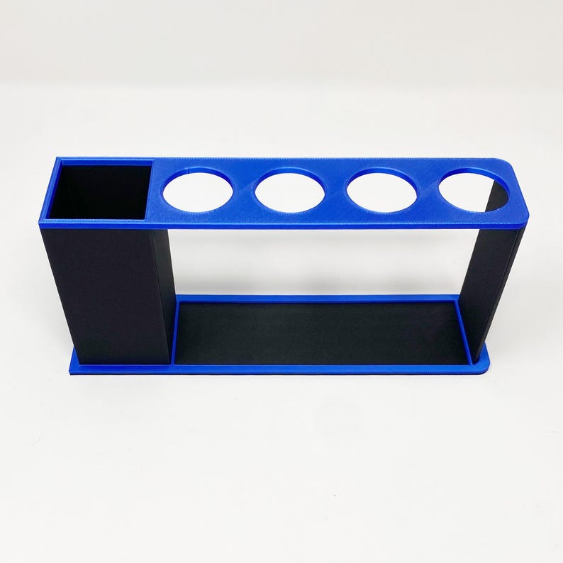 May include: A blue and black plastic organizer with four round slots and a rectangular compartment. The organizer is designed to hold items like pens, pencils, or paintbrushes.