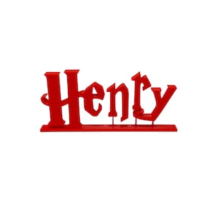 May include: A red, 3D-printed name sign that reads "Henry" in a stylized font. The letters are connected and mounted on a flat base. The sign is designed to stand upright.