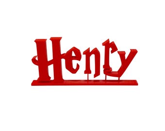 May include: A red, 3D-printed name sign that reads "Henry" in a stylized font. The letters are connected and mounted on a flat base. The sign is designed to stand upright.