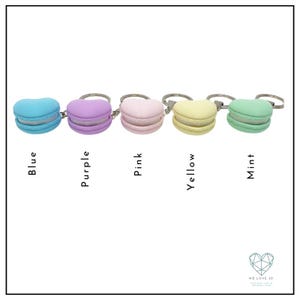 Op de afbeelding: Vijf kleurrijke macaron sleutelhangers in blauw, paars, roze, geel en mintgroen. Elke hanger is gevormd als een macaron met een zilveren sleutelring.