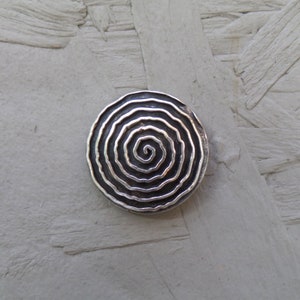 May include: A silver circular pendant with a raised spiral design.