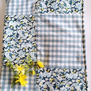 May include: A patchwork quilt featuring a blue and white gingham pattern and a floral design in shades of blue and yellow.