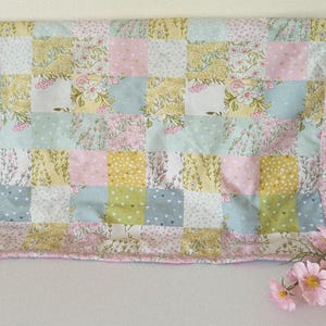 May include: A pastel-coloured patchwork quilt with a floral design. The quilt is made up of squares of pink, yellow, blue, and white fabrics, each with floral and dotted patterns. It has a pink border.