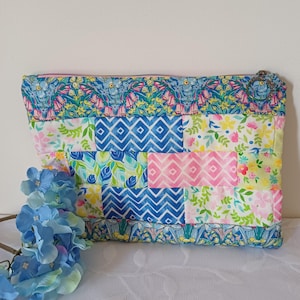 May include: A patchwork pouch with a floral and geometric design. The pouch features a variety of patterns in shades of blue, pink, yellow, and green. It has a zip closure and a floral patterned border.