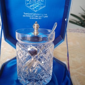 May include: A cut-crystal jar with a silver lid and spoon, presented in a blue box. The jar features a diamond pattern and a Stuart Crystal label. The box reads "Traditional Craftsmanship from the Makers of Finest Lead Crystal Established 1827."