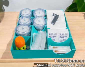 Puede incluir: Un organizador de plástico turquesa con múltiples compartimentos para guardar suministros médicos. El organizador incluye seis contenedores transparentes, dos paquetes de toallitas con alcohol, una jeringa pequeña y un pequeño dispositivo naranja. El texto "T1D3DGEAR.com" y "Suministros médicos NO incluidos" está impreso en la parte inferior del organizador.