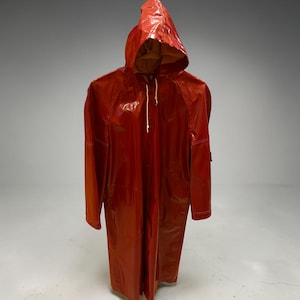 May include: A glossy, deep red raincoat featuring a hood with white drawstring cords. The coat has long sleeves, a front button closure, and a smooth, reflective finish. The interior lining appears to be a contrasting tan or light brown color.