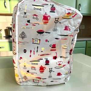 Puede incluir: Una funda para electrodomésticos blanca con un patrón repetitivo de ilustraciones de cocina en rojo, negro y amarillo. El estampado incluye varios artículos como teteras, relojes, batidores, cucharones y utensilios de cocina variados.