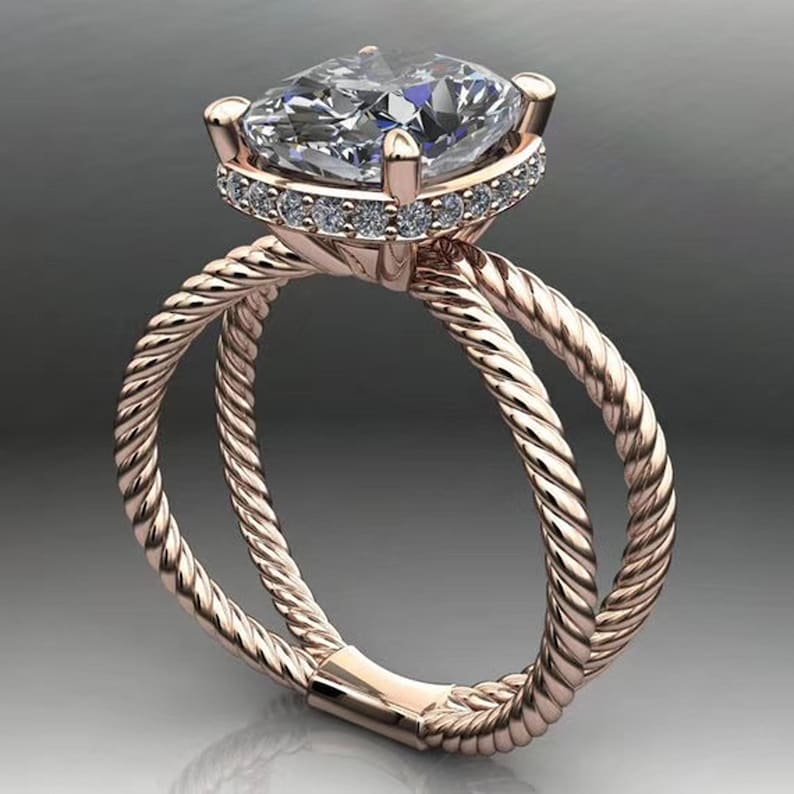 May include: A rose gold engagement ring with a large, clear, cushion-cut center stone surrounded by a halo of smaller diamonds. The band is a double-rope design.