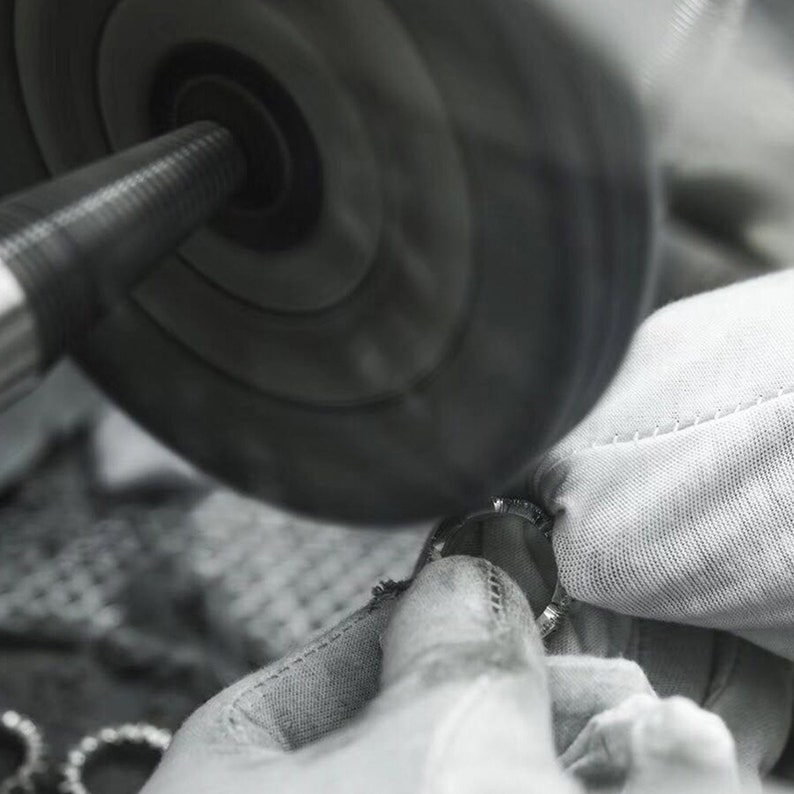 May include: A close-up of a ring being polished by a buffing wheel. The ring is held in a white cloth and the buffing wheel is spinning rapidly.
