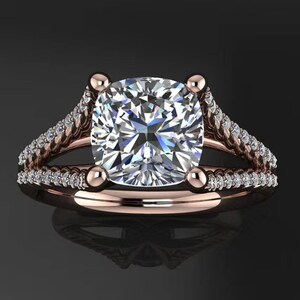 May include: A rose gold engagement ring with a large, square-shaped diamond center stone. The band is adorned with smaller diamonds and features a twisted design.