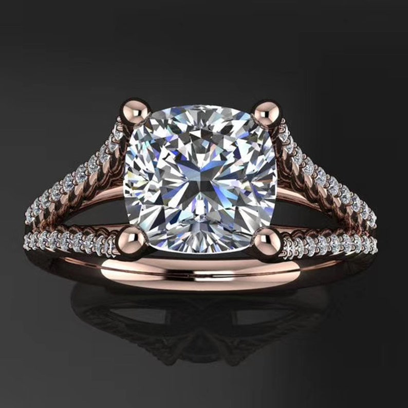 May include: A rose gold engagement ring with a large, square-shaped diamond center stone. The band is adorned with smaller diamonds and features a twisted design.