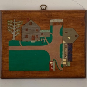 May include: A wooden plaque with a painted scene of a farmhouse and surrounding buildings. The plaque has a green lawn, brown paths, and a small tree. The buildings are painted in shades of brown, gray, and white.