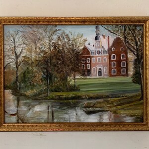 May include: A framed oil painting depicting a red brick building with a clock tower, surrounded by trees and a pond. The building has multiple windows and a central entrance. The painting is set against a backdrop of a blue sky with white clouds.