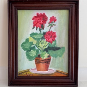May include: Oil painting of a potted geranium plant with vibrant red flowers and green leaves. The painting is in a dark brown wooden frame. The artist's signature, "Almont Young 1940", is visible in the lower left corner.