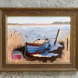 K&ouml;nnte beinhalten: Ein gerahmtes &Ouml;lgem&auml;lde, das ein blaues und rotes Holzboot zeigt, das an einem Seeufer angelegt ist. Das Boot ist an einem Holzpfosten festgemacht und von hohen Schilf umgeben. Das Wasser ist hellblau und der Himmel ist hellblau. Das Gem&auml;lde ist in einem goldenen Rahmen gerahmt.