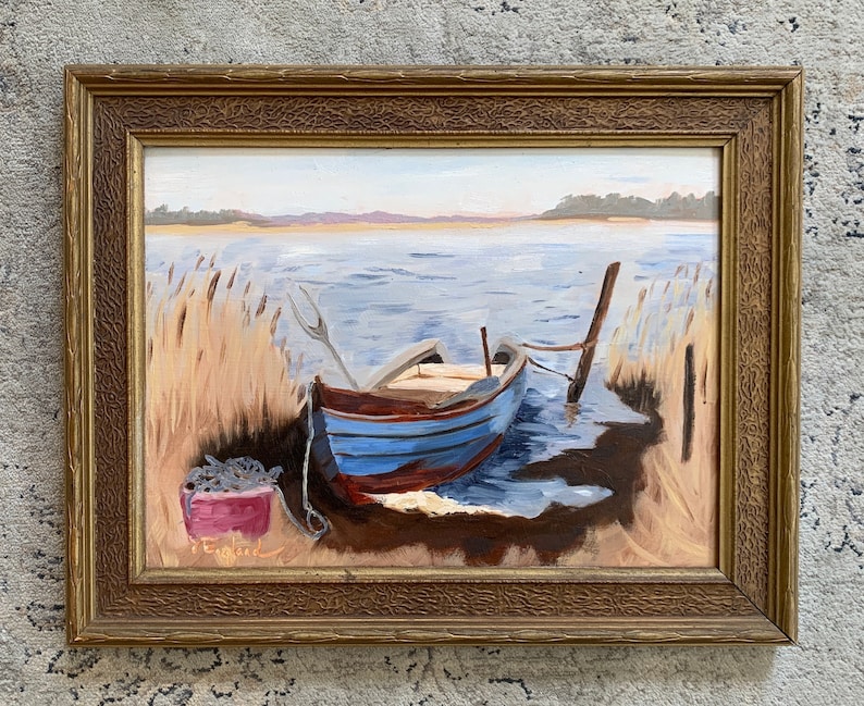 K&ouml;nnte beinhalten: Ein gerahmtes &Ouml;lgem&auml;lde, das ein blaues und rotes Holzboot zeigt, das an einem Seeufer angelegt ist. Das Boot ist an einem Holzpfosten festgemacht und von hohen Schilf umgeben. Das Wasser ist hellblau und der Himmel ist hellblau. Das Gem&auml;lde ist in einem goldenen Rahmen gerahmt.