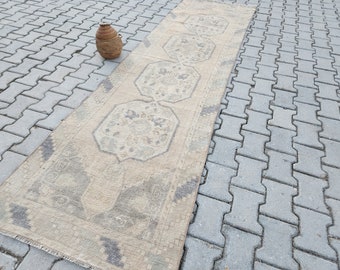Könnte beinhalten: Ein hellbeiger Läuferteppich mit einem verblassten grauen Muster. Der Teppich hat ein geometrisches Design mit sich wiederholenden Achtecken und floralen Motiven. Der Teppich liegt auf einer grauen Steinplatte.