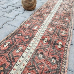 May include: A long, narrow rug with a traditional Persian design. The rug has a red background with a white and brown geometric pattern. The rug is perfect for adding a touch of traditional style to any room.