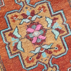 May include: A close-up of a colorful rug with a geometric pattern. The rug is made of woven fabric and has a variety of colors, including red, orange, blue, and green.