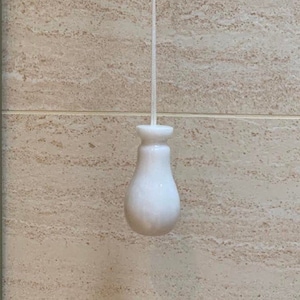 Może przedstawiać: Biały ceramiczny włącznik światła z sznurkiem zwisającym z sufitu na tle beżowych płytek.