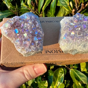 May include: Two amethyst crystal clusters with iridescent rainbow colours. The crystals are on a brown box with the text "STONE KING" and "IN CHINA SP" printed on it.