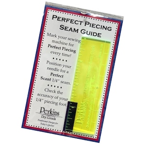 May include: A clear, yellow Perfect Piecing Seam Guide with black and white measurements, packaged in a clear plastic sleeve. The packaging features text in red, white, and blue, including "Perfect Piecing Seam Guide" and "Perkins Dry Goods."