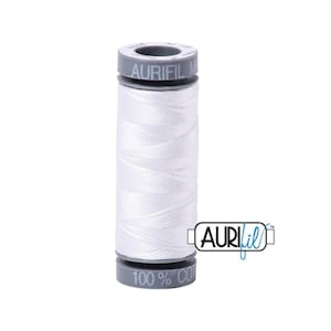 May include: A spool of white Aurifil thread, 100% cotton, with a gray label that reads "Aurifil 50 wt 1200 yd 1100 m".