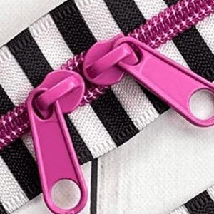 May include: A zipper featuring two bright pink pulls and a matching pink coil track. The zipper tape is decorated with a repeating pattern of bold black and white vertical stripes, providing a high-contrast look for this functional fastener.