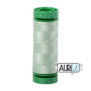May include: A spool of light green thread with the brand name "Aurifil" printed on the spool. The spool is made of plastic and has a green cap.