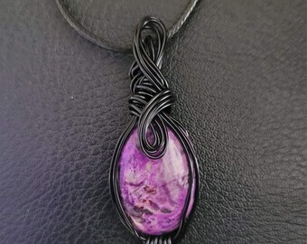 May include: A purple and white agate stone pendant wrapped in black wire, hanging from a black cord.