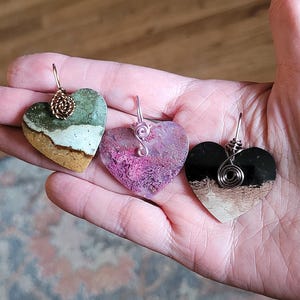 Può includere: Tre ciondoli a forma di cuore in pietra naturale con dettagli in filo avvolto. Le pietre sono verdi, rosa e nere con accenti bianchi.