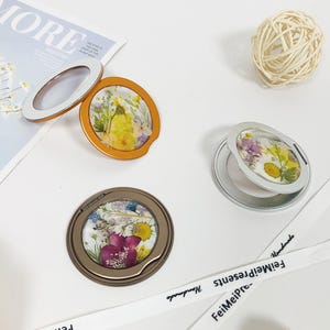 May include: Three round, silver-toned, handheld mirrors with a floral design. Each mirror has a different floral pattern pressed into the surface. The mirrors are on a white surface.