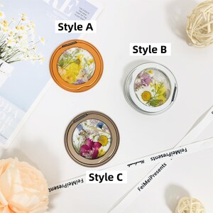 May include: Three round, decorative phone grips with different styles of pressed flowers. The phone grips are in orange, white, and gold frames. The text "Style A", "Style B", and "Style C" are written below each phone grip.